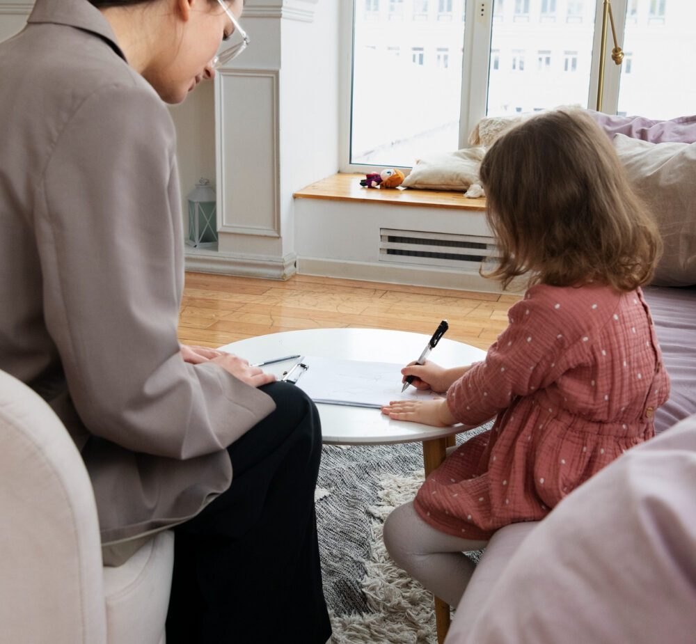 Occupational therapist sitting with a young girl as she writes at a small table