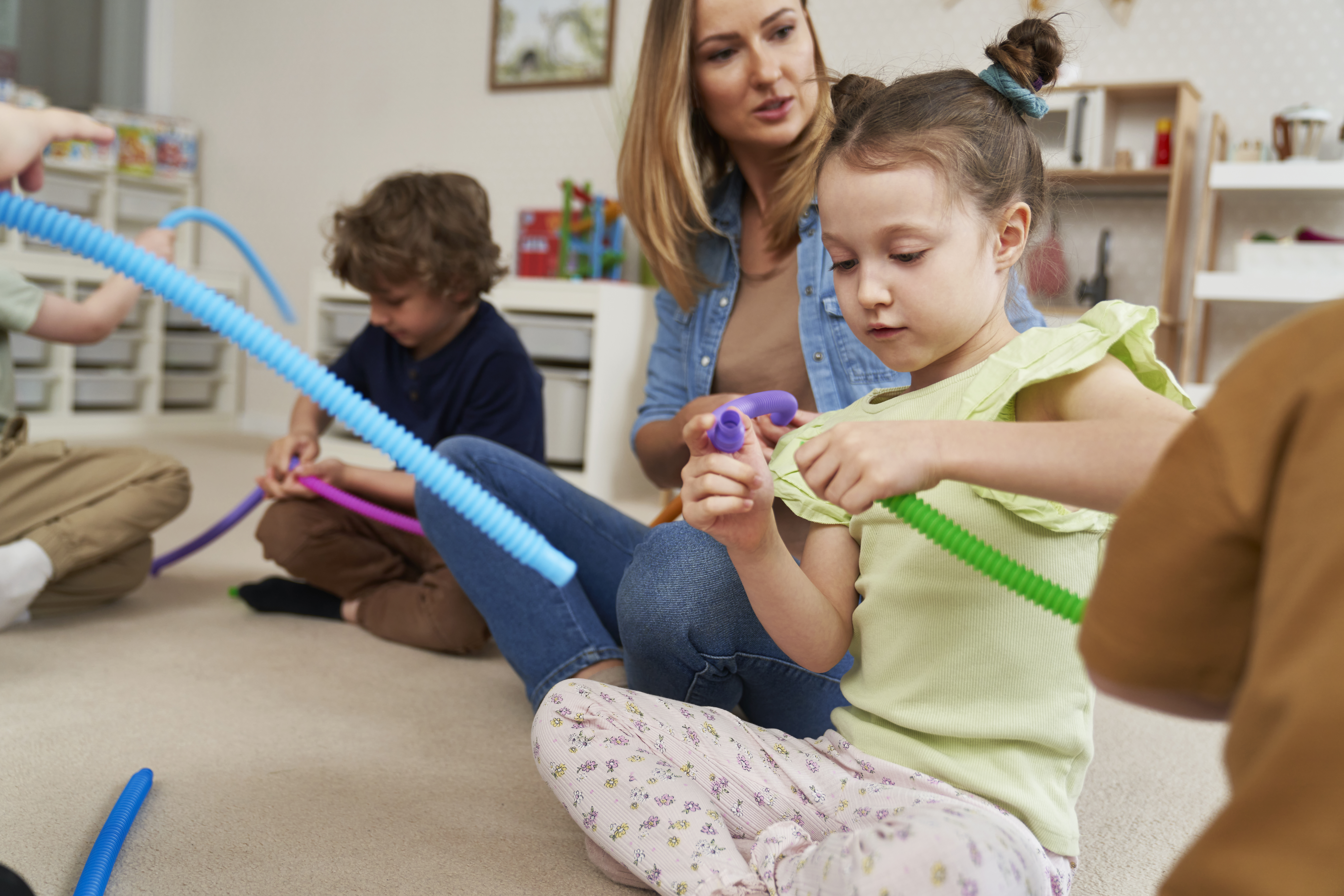 therapist on the floor with a small group of preschoolers doing a hands-on fine motor activity